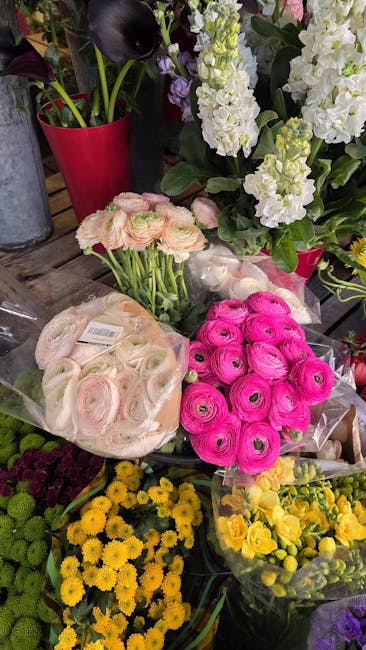 A vibrant display of fresh flowers at flowersharmondsworth.co.uk, featuring pink ranunculus and pale pink spray roses arranged in clear plastic sleeves, surrounded by clusters of yellow chrysanthemums