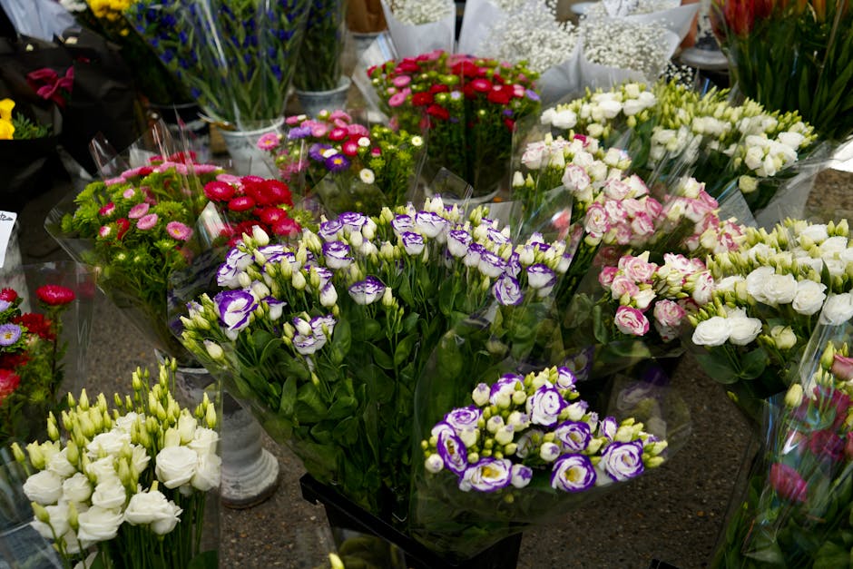 A vibrant display of freshly arranged floral bouquets featuring a variety of flowers including purple and white lisianthus, pink and white roses, red and pink daisies, and other mixed blooms. The flow